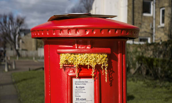 A red mailbox with noodles overflowing out of the mail/letter slot.