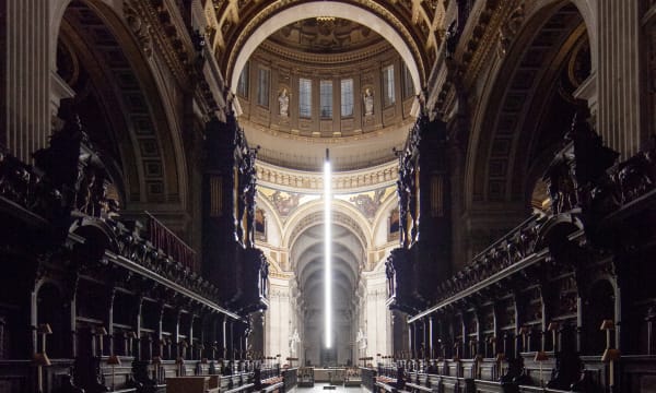 Interior of darkened cathedral nave with long thin column of white light coming from the dome above