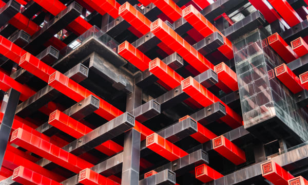 Modern building facade featuring repeating interlocking black and bright red geometric panels with square ventilation grilles