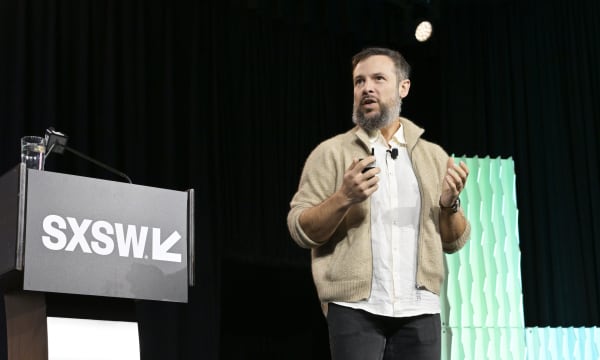 Aza Raskin on stage at SXSW 2026. He wears a beige casual jacket, white shirt and black jeans and is gesturing with his hands.