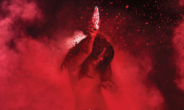 Woman dancing in red dust holding a white Coca-Cola bottle