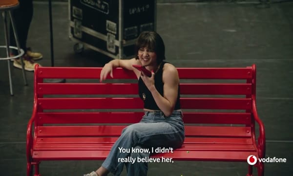 A women sitting on a red bench holding a phone speaking into it