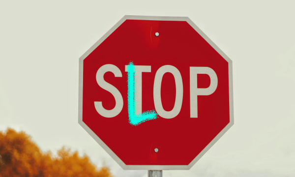 Red stop sign edited with blue pen to turn the letter 'T' into an 'L' to instead spell 'Slop'.
