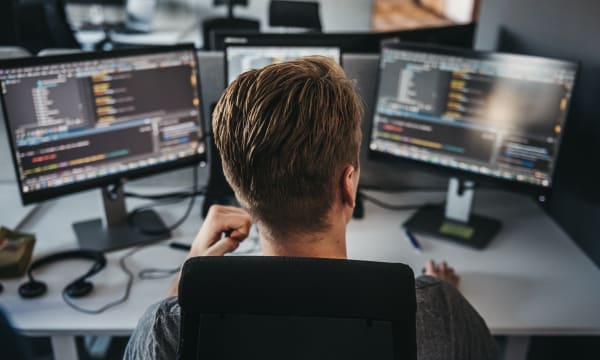 person in front of three computer screens