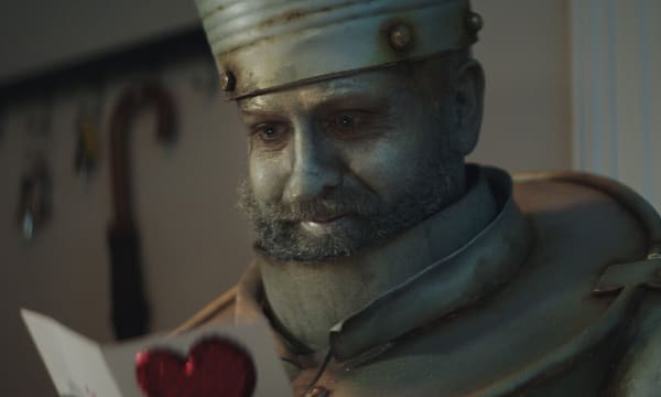 Man dressed as a silver Tin Man smiling whilst opening a Christmas card with a red heart symbol on the front