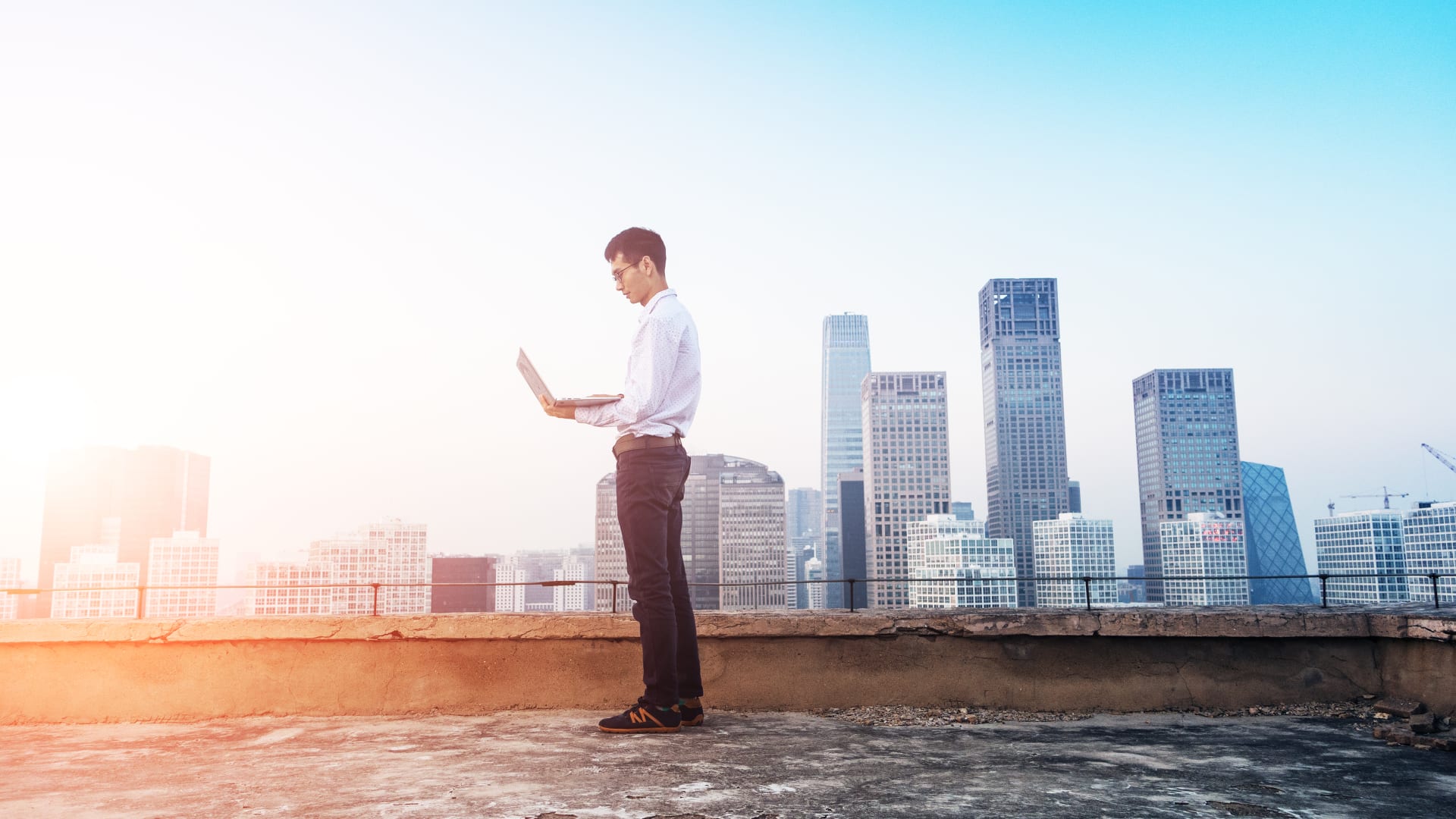 Man standing on a city roof with laptop