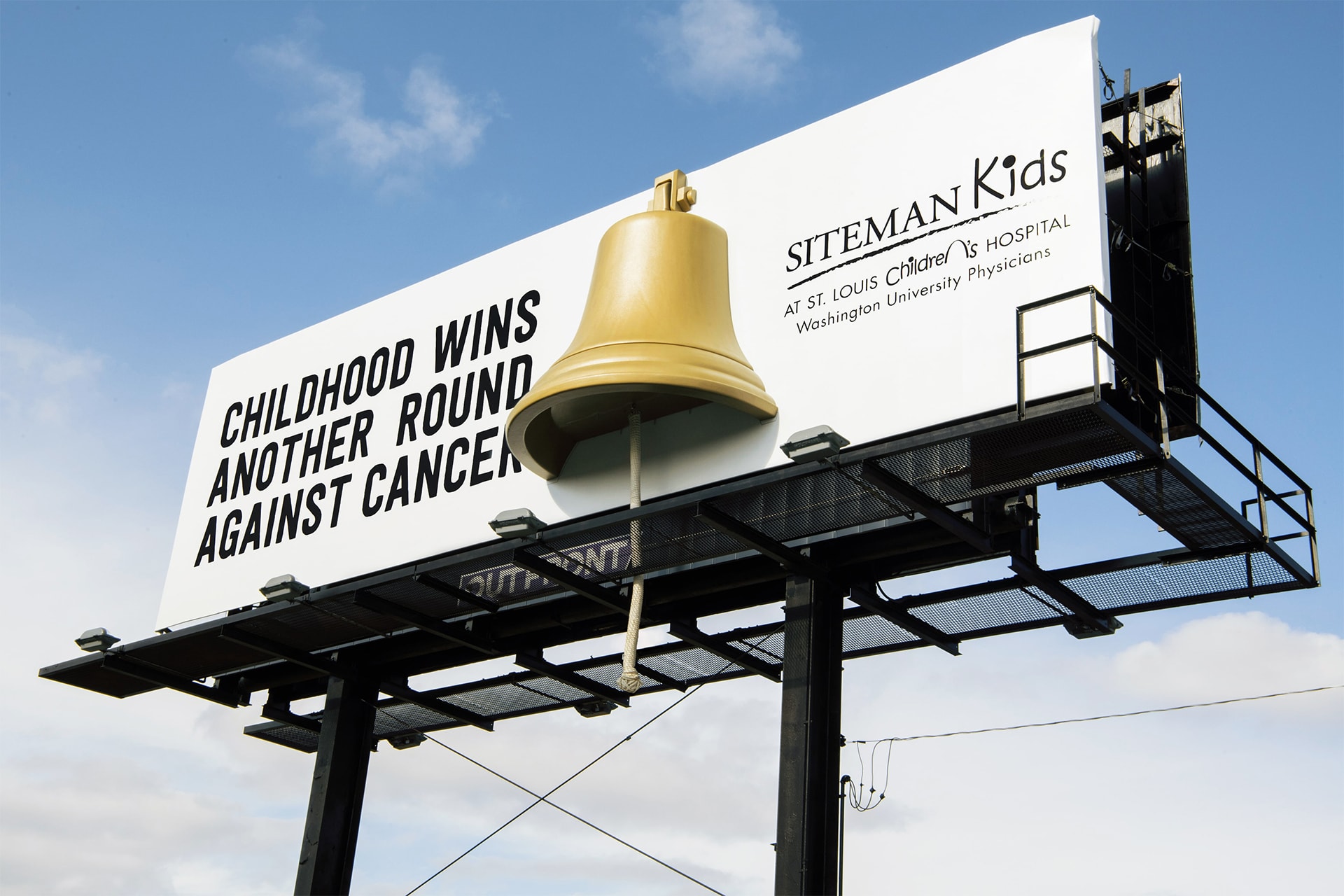 Blue sky, with a billboard in the for front with a 3-D bell. Childhood wins another round against cancer.