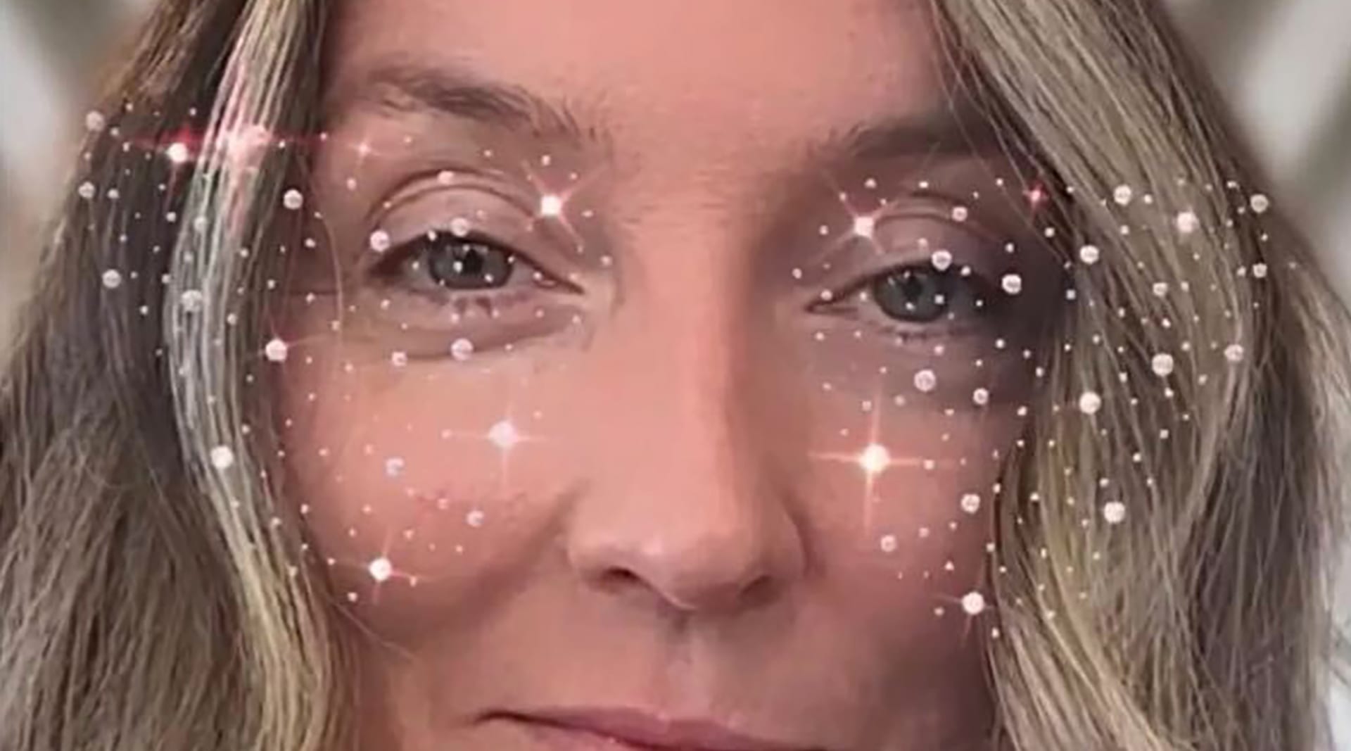 A blonde woman stares into the camera, only her eyes and nose showing, with a digital overlay of stars and sparkles accenting her eyes.