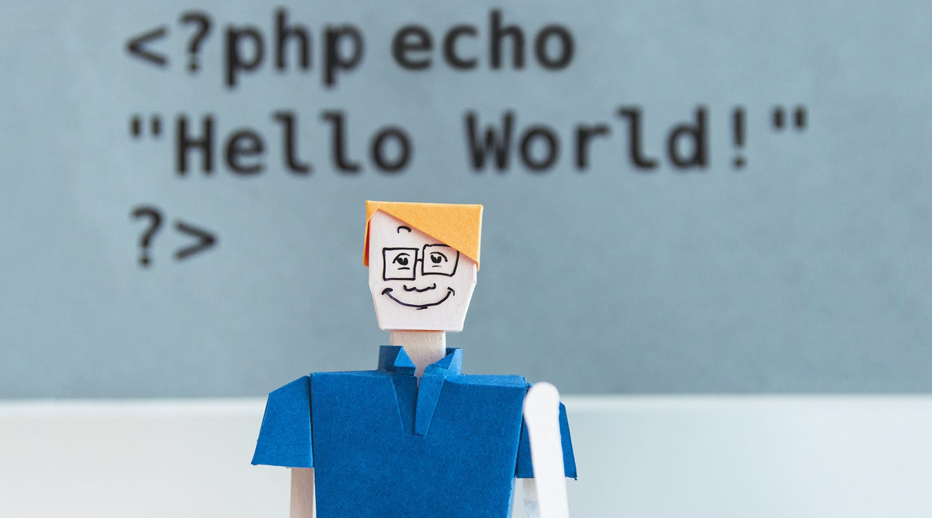 A digitally-rendered cartoon man with yellow hair, a blue shirt smiles at the camera. Behind him, a set of code: <?php echo "Hello World!" ?>