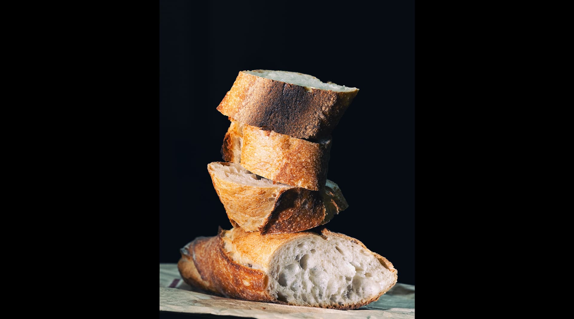 Four slices of baguette, cut diagonally, are stacked on top of each other in front of a black backdrop.