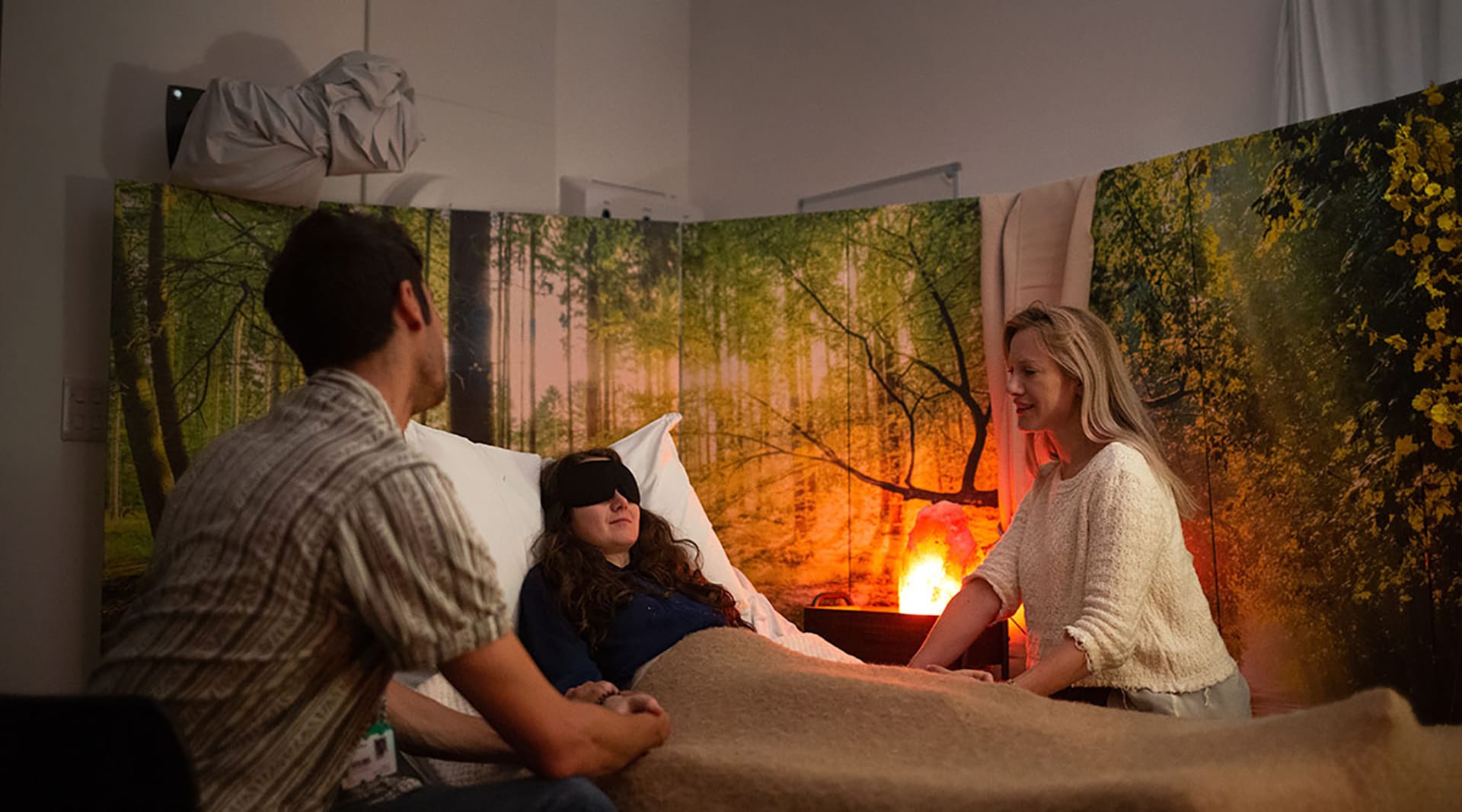 A blindfolded person sitting in a bed with a therapist sitting on either side of the bed.