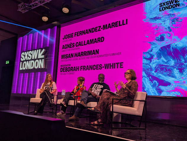 A low-angle shot of four panel speakers on stage under bright pink screens at a SXSW London event.