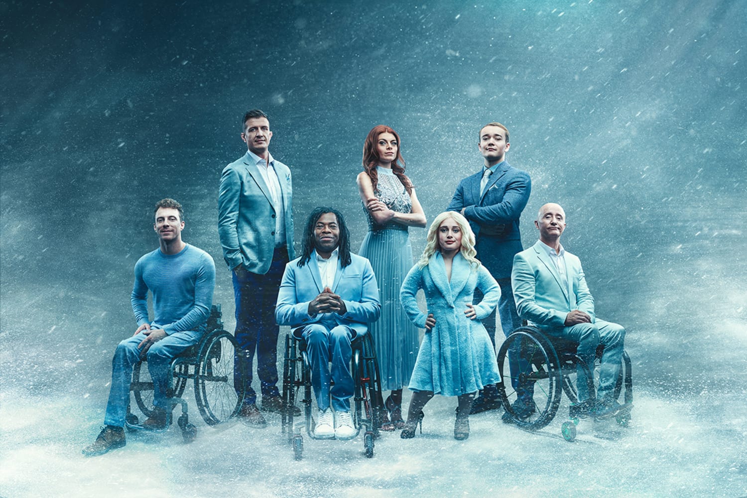 Seven people with different disabilities pose against a light blue background surrounded by swirling snow. They are all wearing blue clothing. Four are standing, while three are seated in wheelchairs.