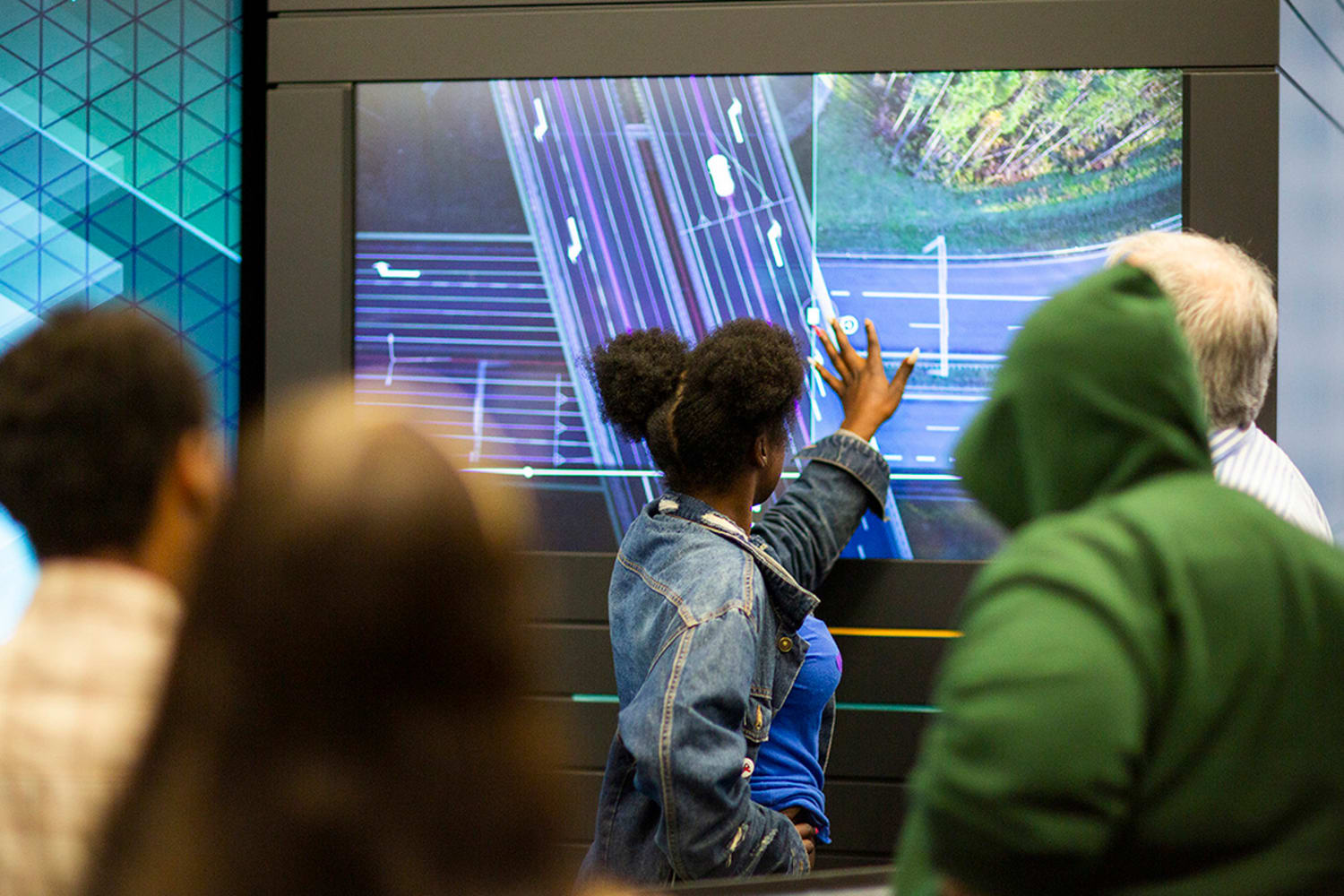 A woman with dark curly hair demonstrates mapping for autonomous vehicles to a group of onlookers.