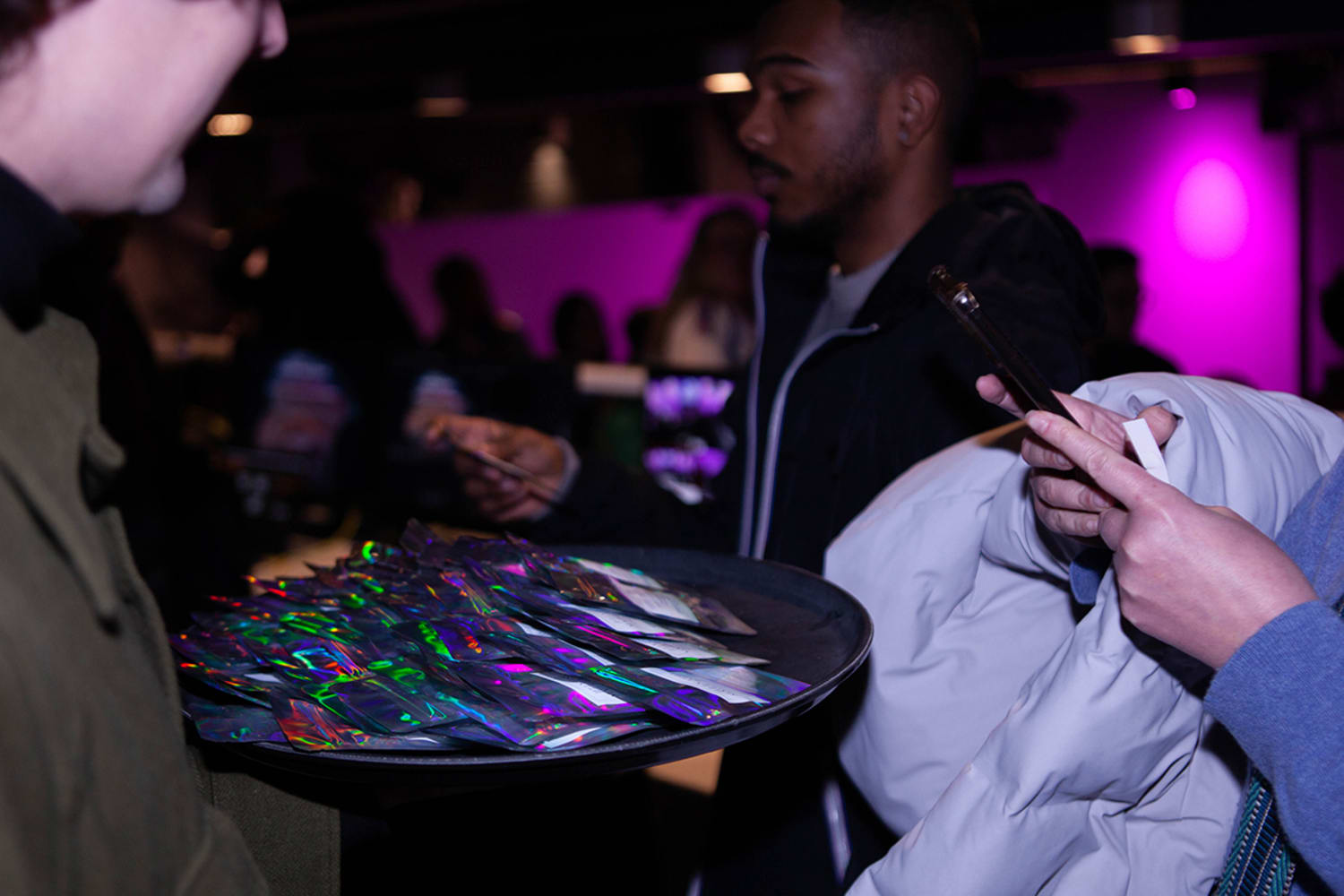 A man holds a black tray of black and neon-wrapped snacks.