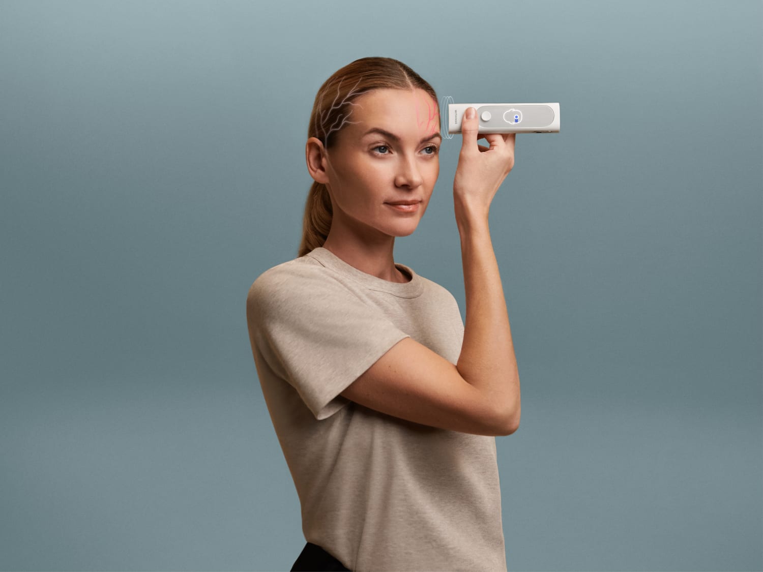 A blond white woman in a light t shirt holds a small rectangular device to her forehead