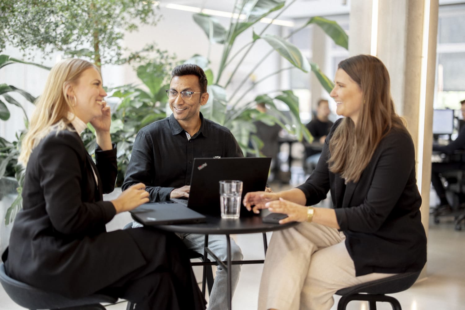 Image of 3 coworkers in our MAP office, sat at a table and laughing and conversing