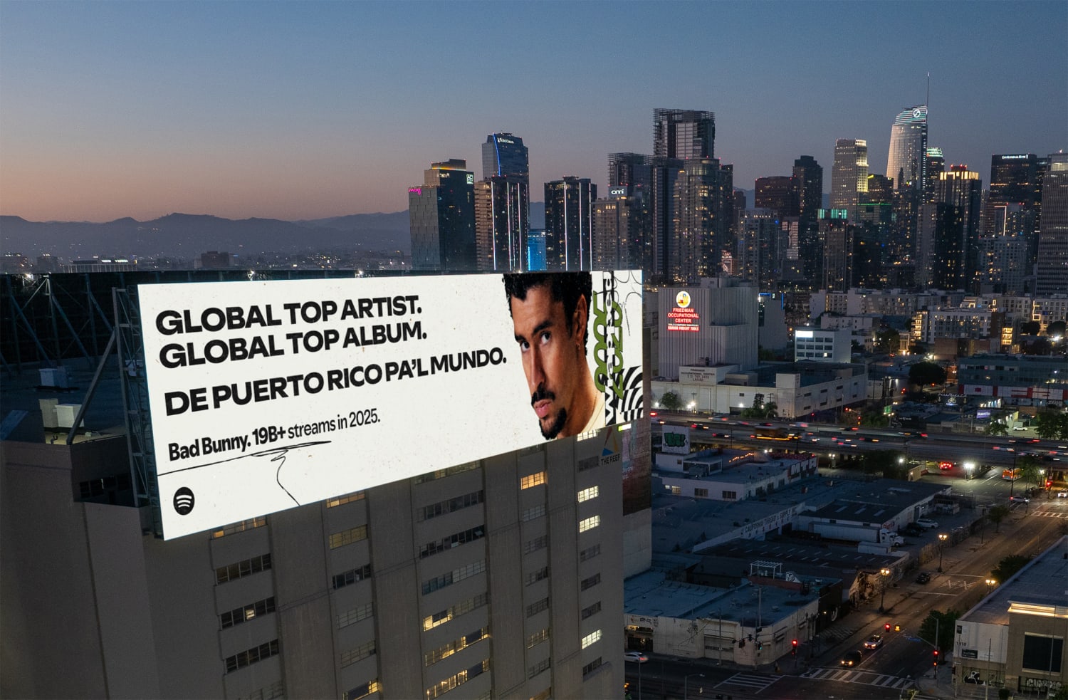 A city skyline at dusk with a building wrapped by a billboard showing Bad Bunny as Global Top Artist 2025.