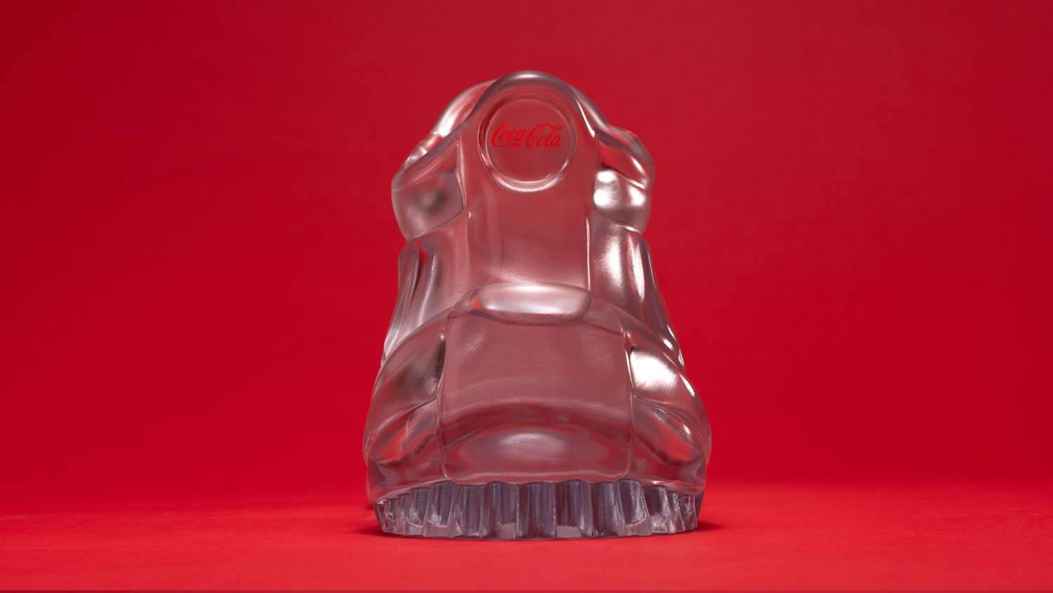 A back heel view of a transparent glass sculpture shaped like a sneaker, displayed against a solid red background.