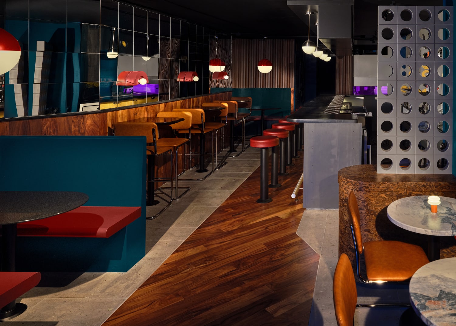 Dark retro bar interior with teal colored booths, wood paneling, circular tables and circular design cues throughout.