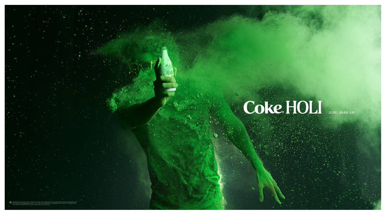 Participant covered in green Holi colours holding a white Coca Cola bottle