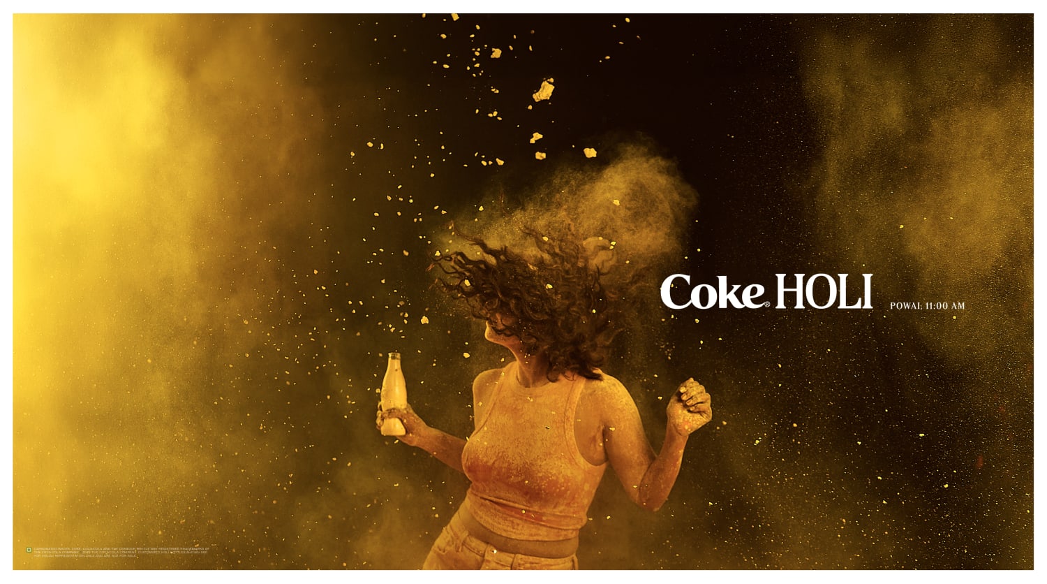 Woman celebrating Holi with yellow colour powder holding a Coca Cola bottle