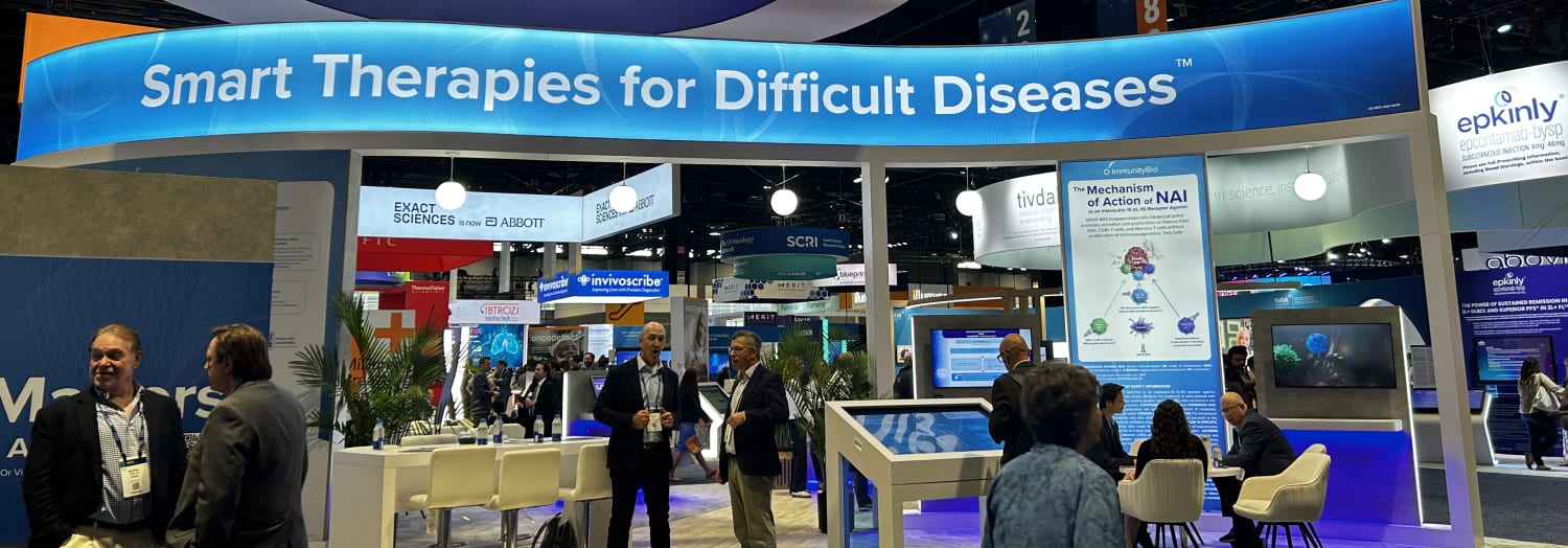 Busy medical exhibition booth with a large blue banner reading 'Smart Therapies for Difficult Diseases' and people.