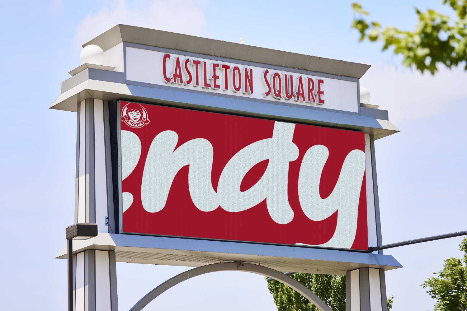 Image of a Wendy's billboard zoomed in on the Wendy's logo so it shows 'Indy' and a logo for Castleton Square above. Trees and a blue sky are behind the billboard.