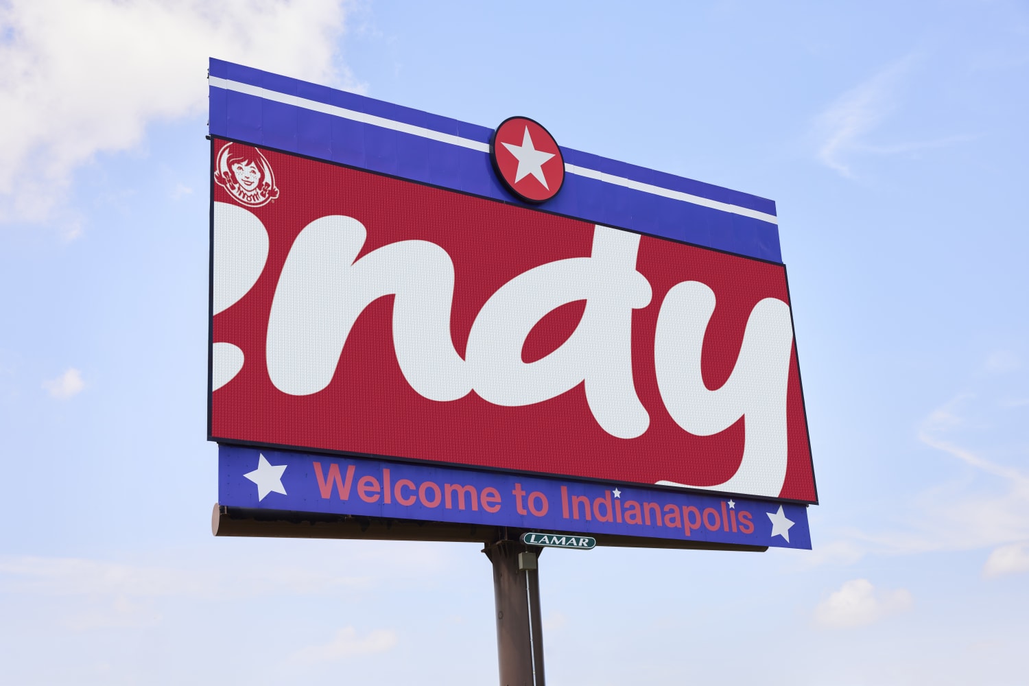 Image of a Wendy's billboard zoomed in on the Wendy's logo so it shows 'Indy'. Below the billboard is text that says "welcome to Indianapolis." Trees and a blue sky are behind the billboard.