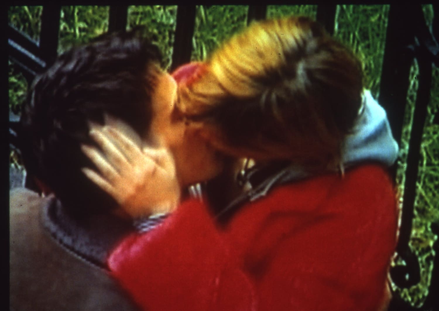 A vintage 1980s image of a couple kissing by some railings.
