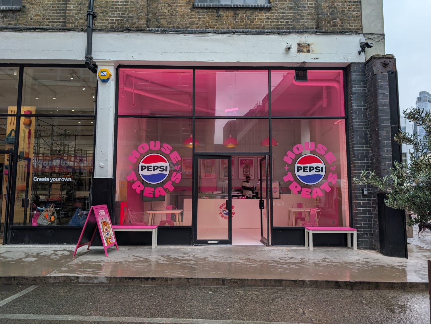 A storefront with pink-tinted windows featuring "House of Pepsi" logos on either side of the entrance on a rainy street.