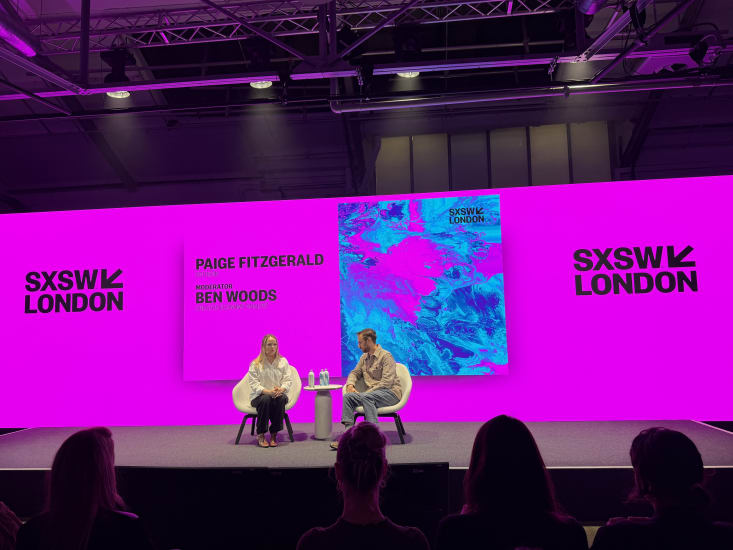 Two people sit on the SXSW London stage in conversation against a bright pink backdrop