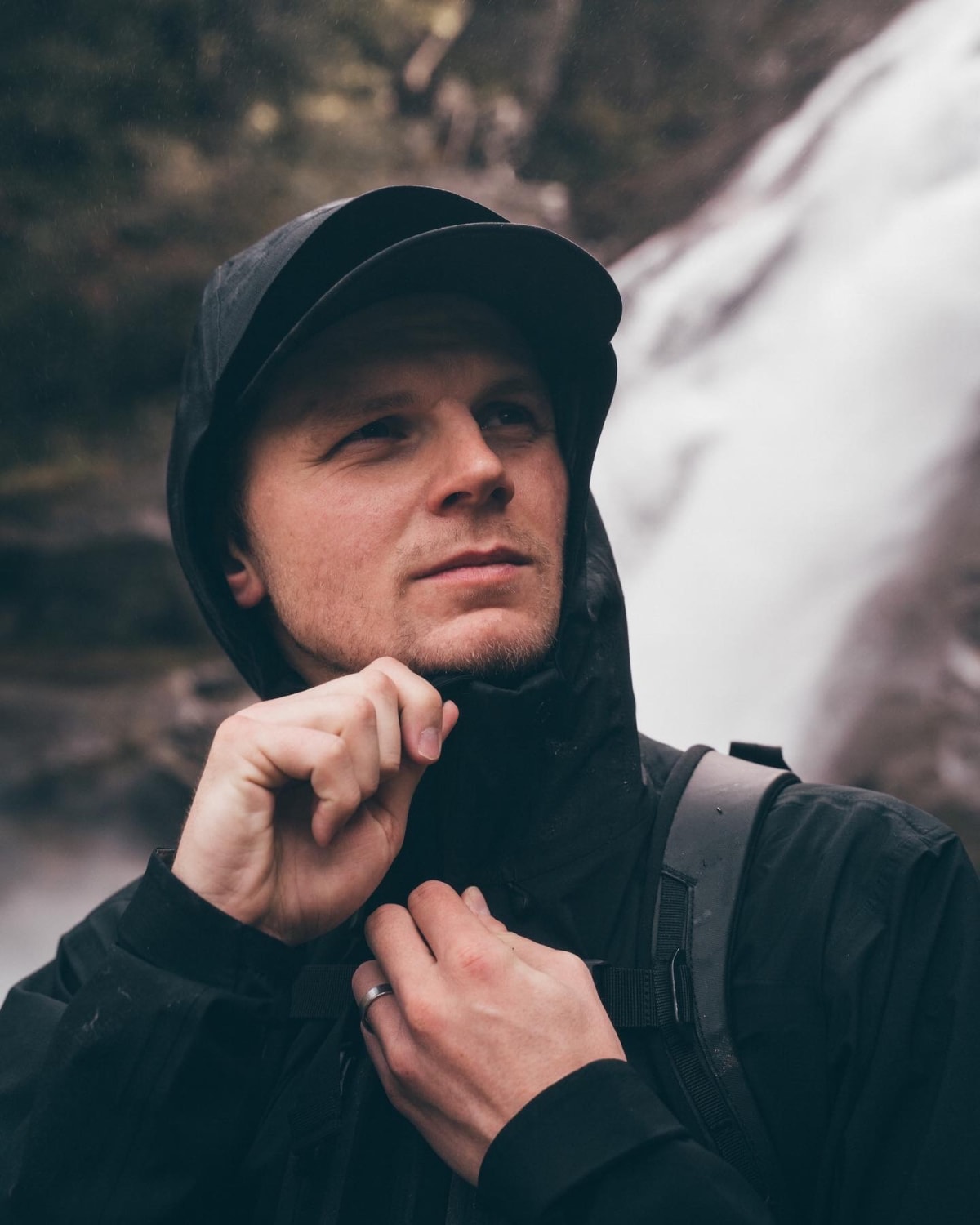 Jamie Nicholls beside a waterfall in a hooded jacket