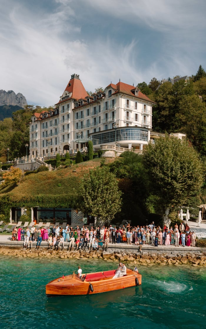 A wooden boat on Lake Annecy below the Palace de Menthon, guests gathered along the quayside