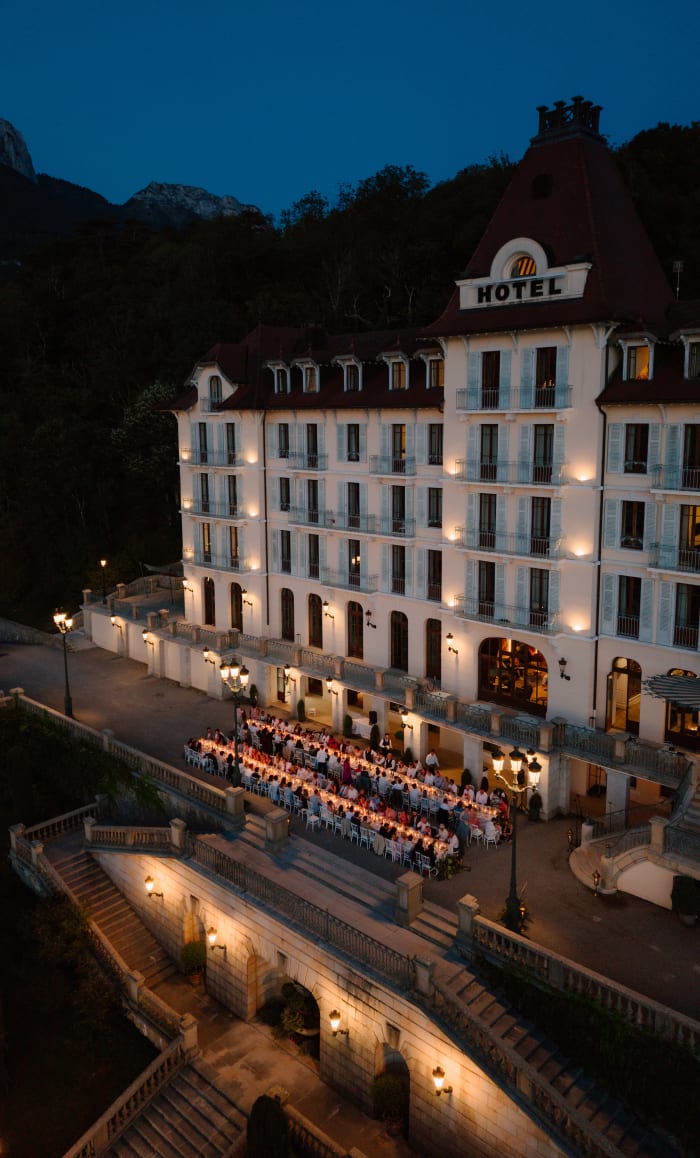 The wedding party dining at a long candlelit table outside the Palace de Menthon after dark, the mountains behind