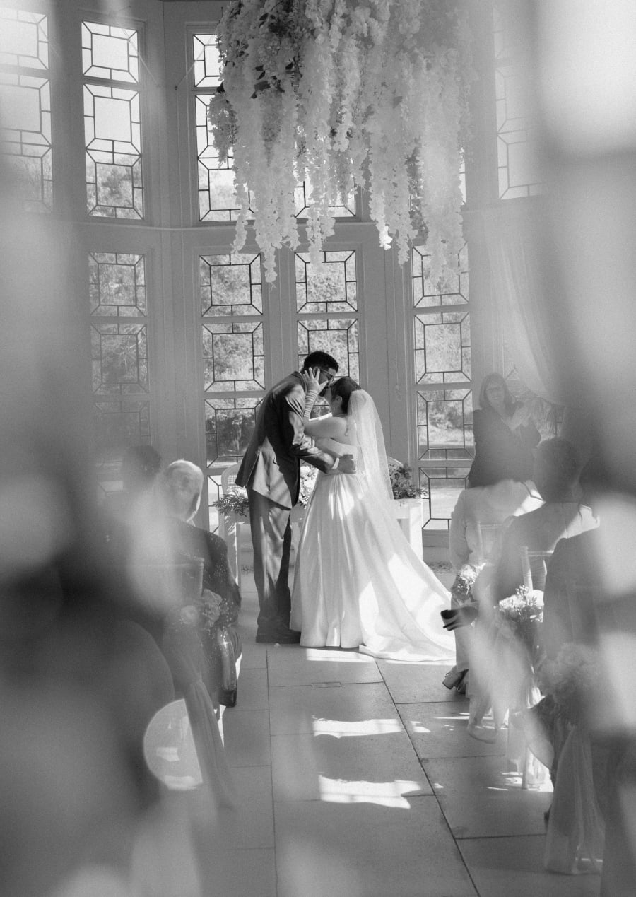The couple framed by the tall windows during the ceremony, in black and white, Highcliffe Castle, Christchurch