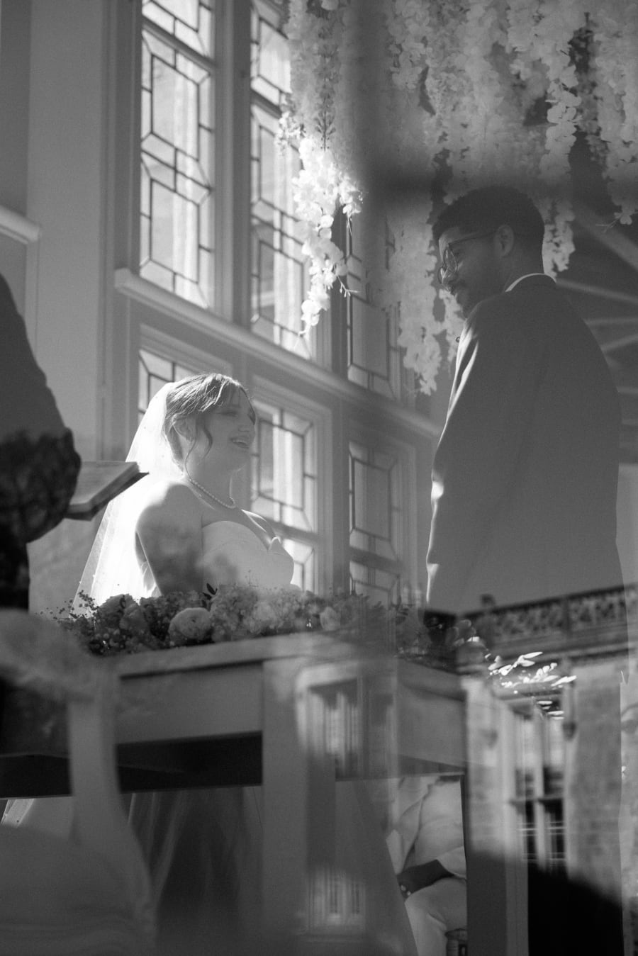 The bride at the ceremony table, caught in the window light, in black and white, Highcliffe Castle, Christchurch