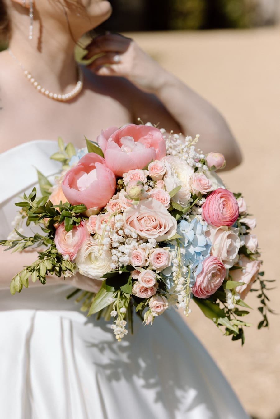 The bridal bouquet of peonies and roses held against her dress, Highcliffe Castle, Christchurch