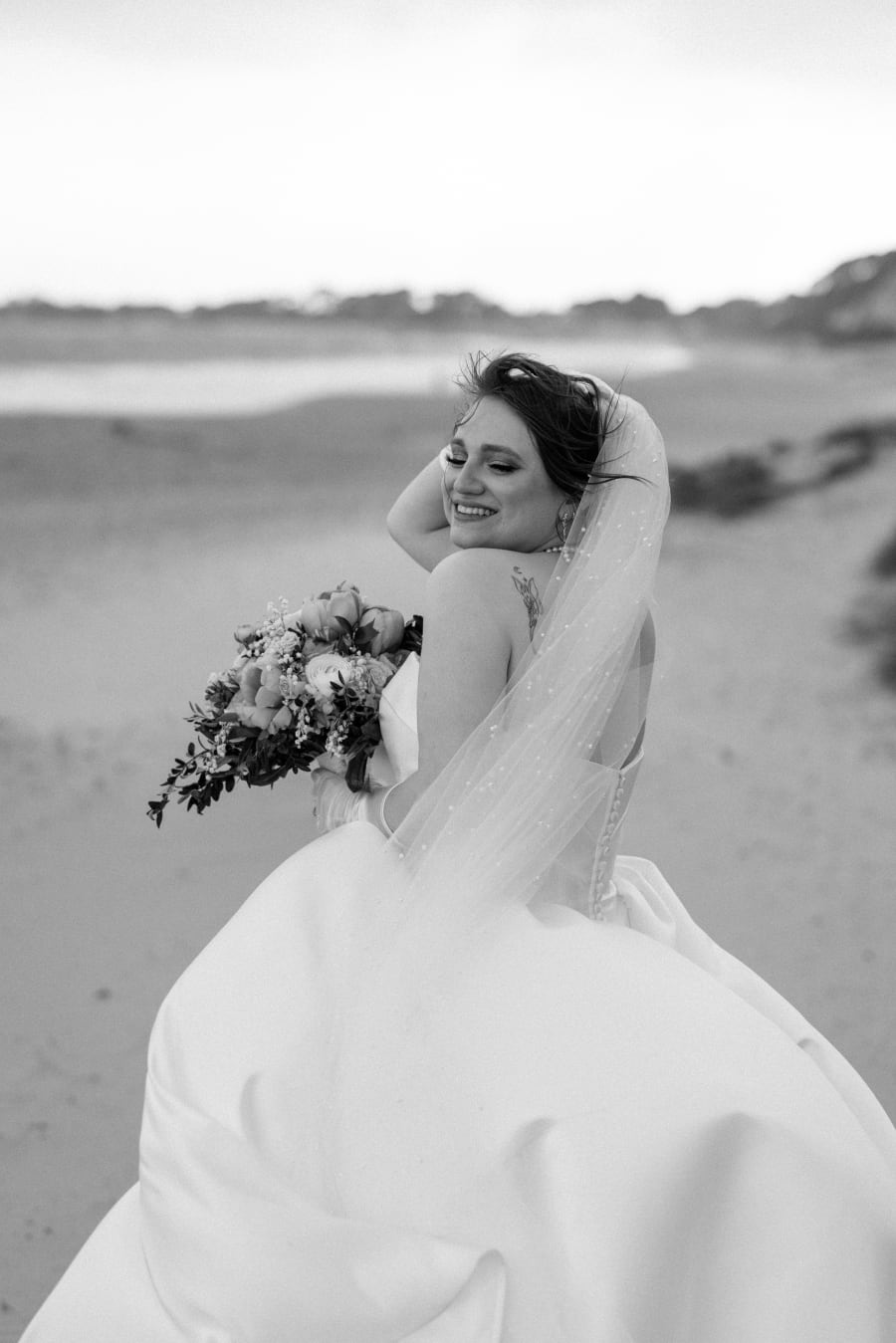 The bride glancing back over her shoulder on the beach, in black and white, Highcliffe Castle, Christchurch