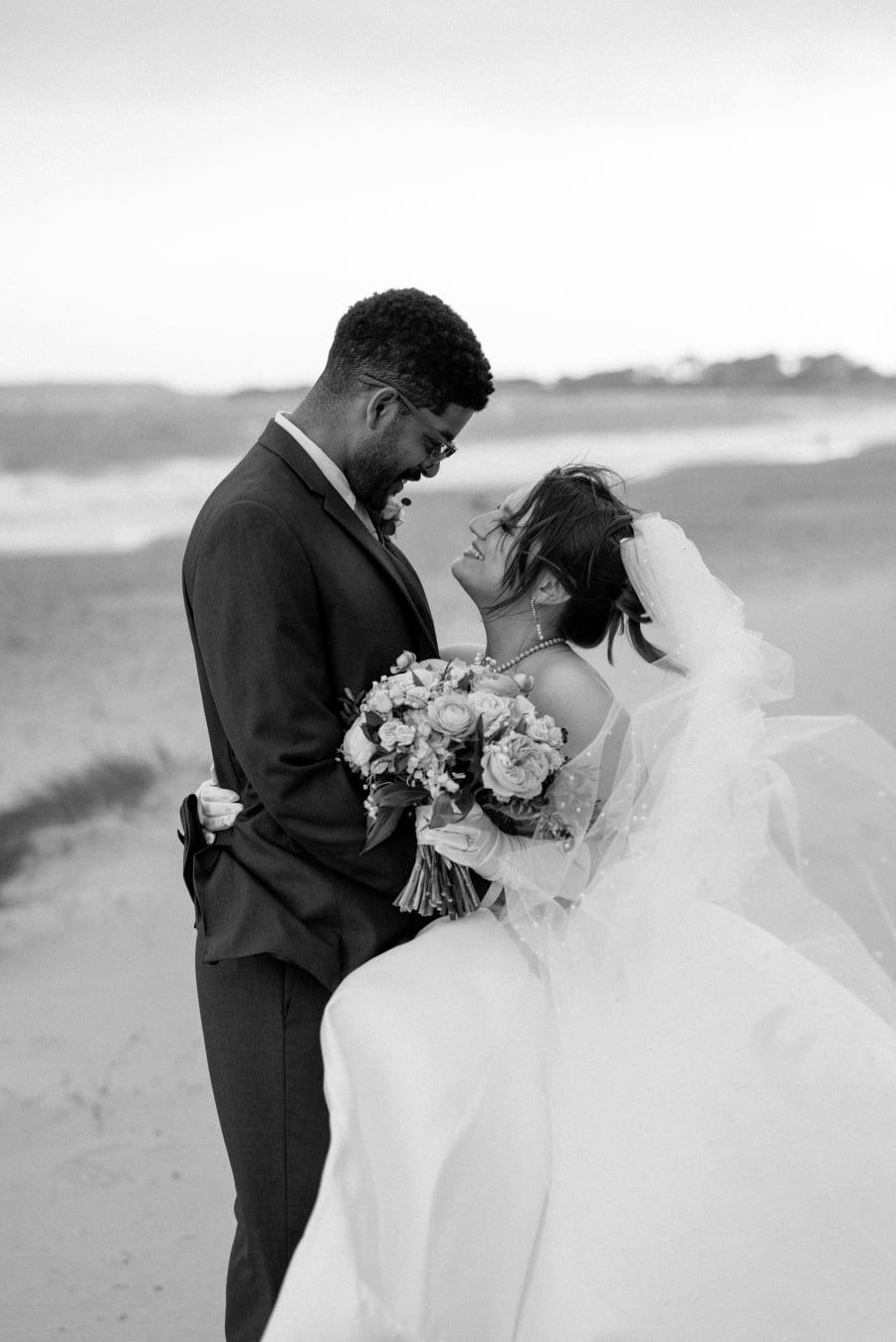 Karter and Ernzo close together on the beach with her bouquet, in black and white, Highcliffe Castle, Christchurch