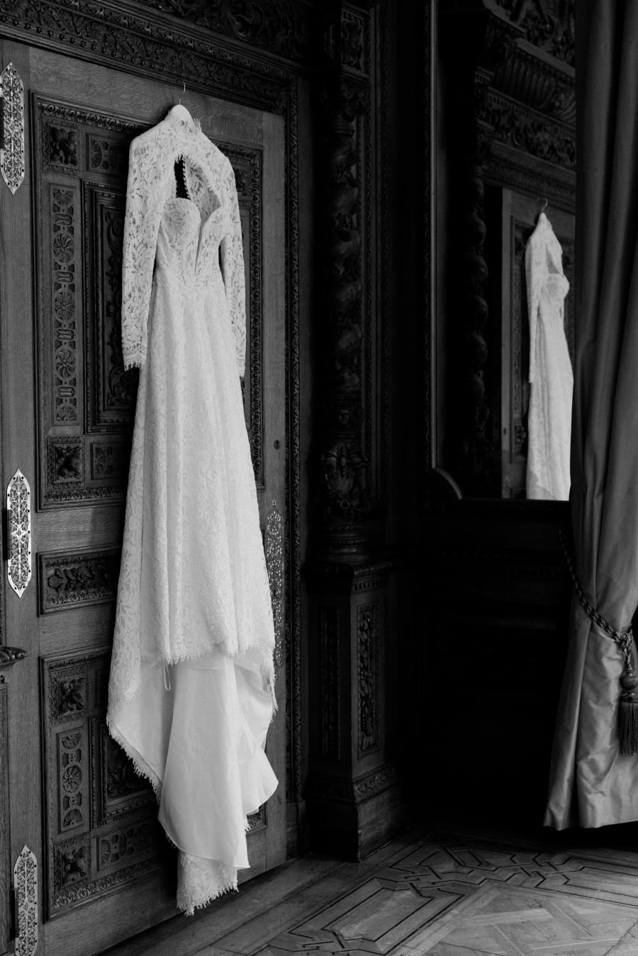 The wedding dress hanging on a carved door before the ceremony, in black and white, The Cotswolds