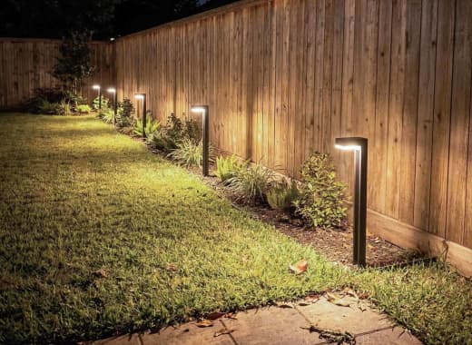 True Lumens™ solar bollard lights along a residential fence line with warm dusk-to-dawn glow at night