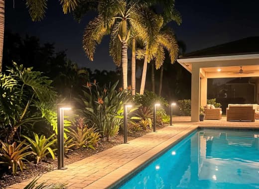 True Lumens™ solar bollard lights beside a pool with warm 3000K amber glow at night