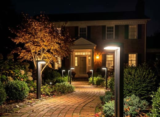 True Lumens™ solar bollard lights lining a paver stone walkway with warm dusk-to-dawn glow