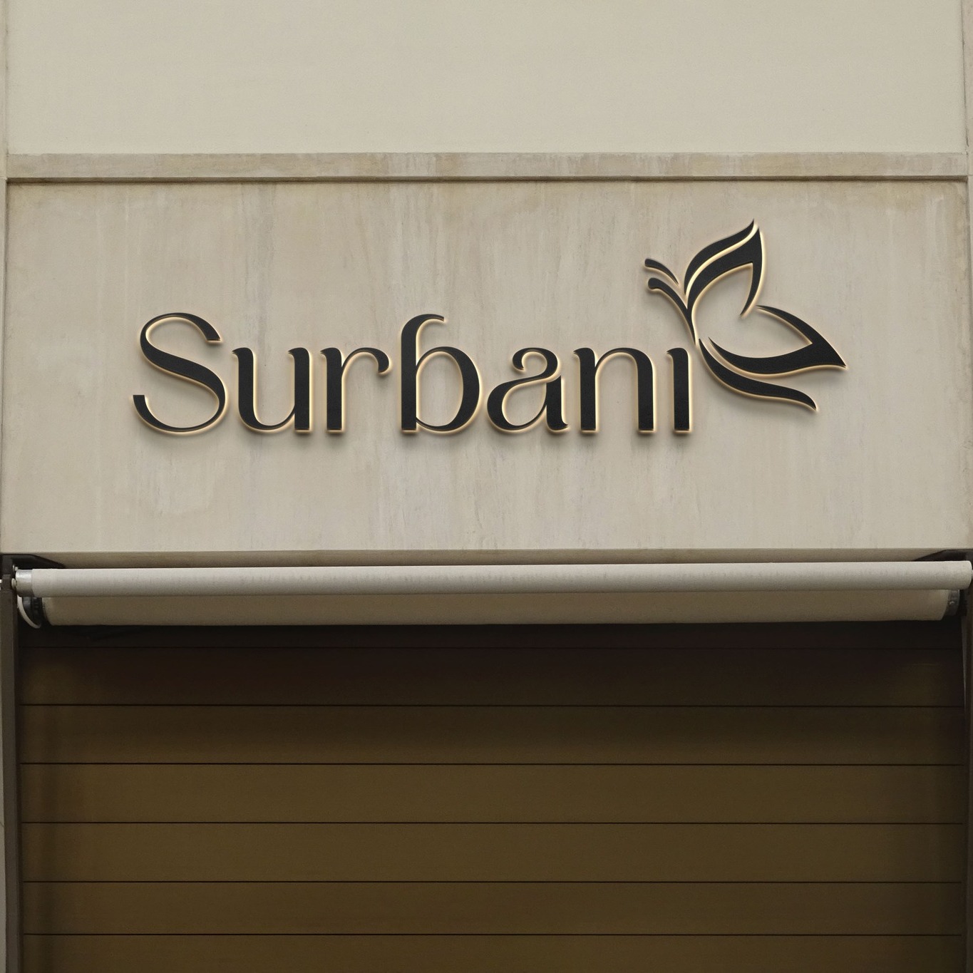 Gold 3D Surbani logo with butterfly icon on a boutique storefront