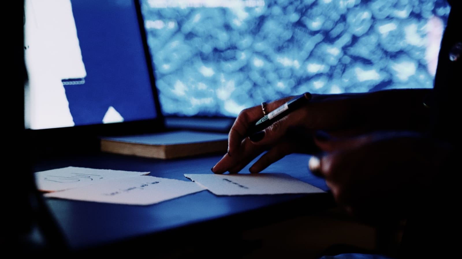 A hand holds a pen over paper on the installation desk, with a blue spatial image in the background.