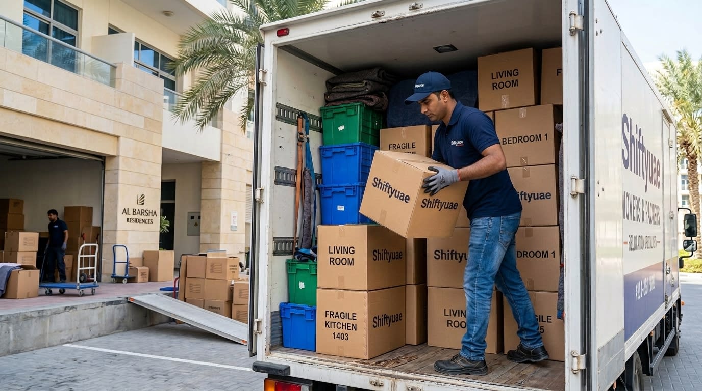 Professional mover stacking double-wall moving boxes and plastic crates inside a moving truck at a Dubai residential building