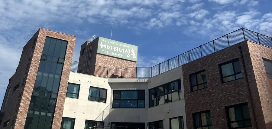 구름 낀 하늘 아래 벽돌·흰 벽 3층 건물과 옥상 간판