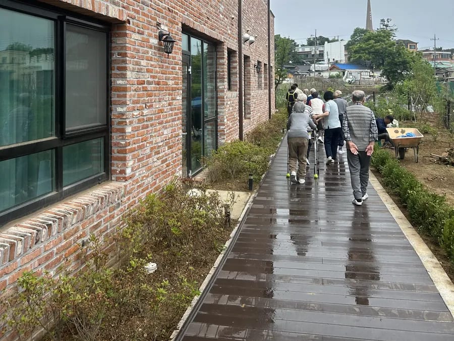 벽돌 건물 옆 데크 길, 멀리 산책하는 어르신들