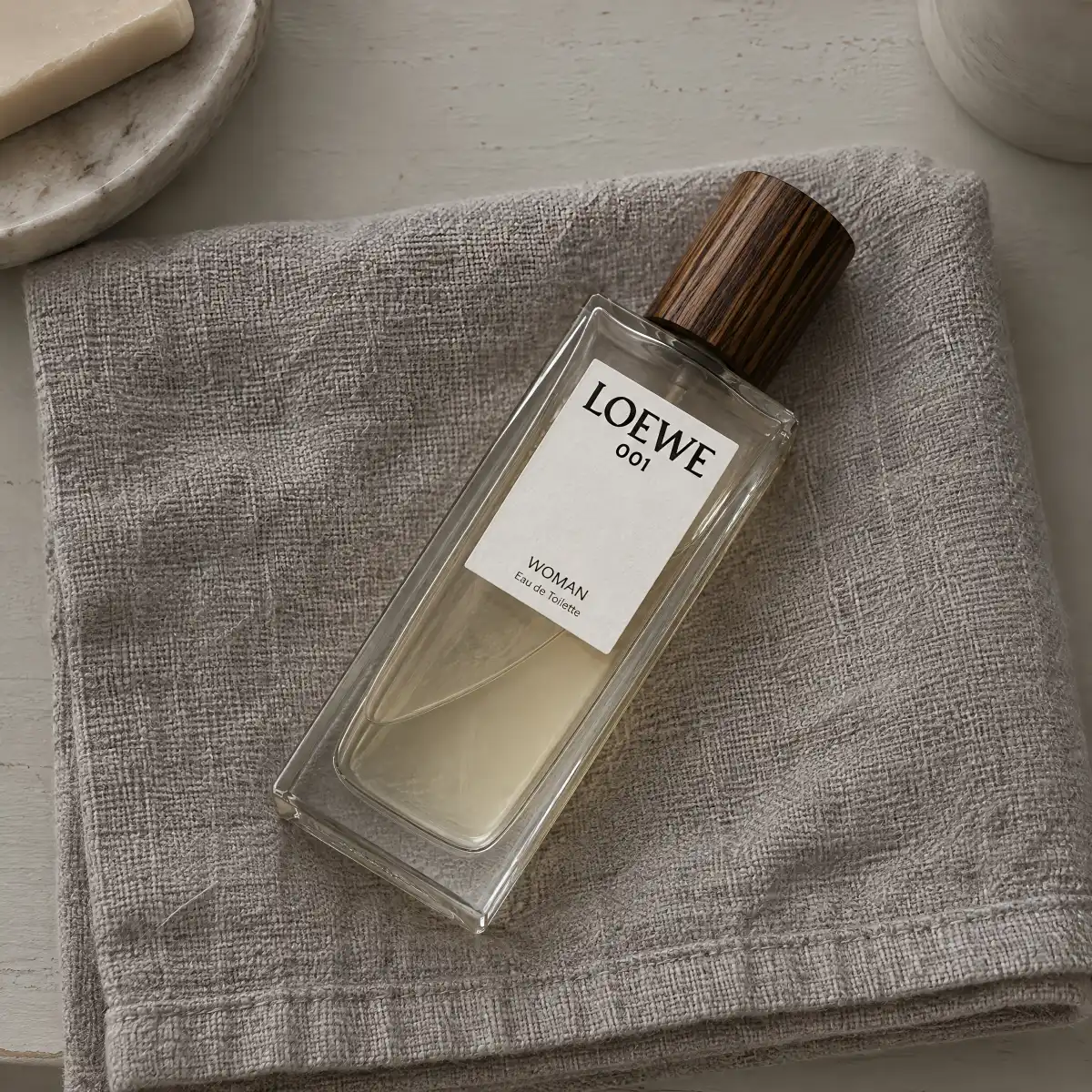 A perfume bottle lying on a folded gray towel beside a bathroom sink